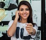 Young woman smiling with earphones in front of a graffiti wall, showcasing urban fashion.